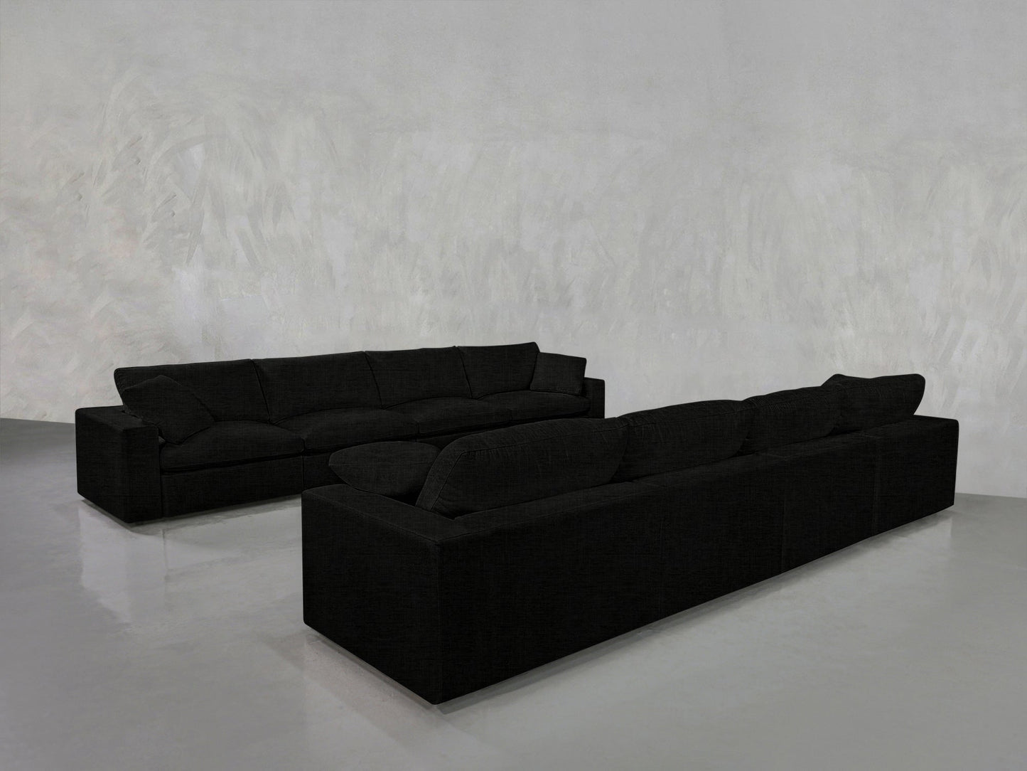Two 4-4 Sofa Sets in modern black are placed opposite each other in a minimalistic room with light gray textured walls and a glossy, reflective floor. The space is empty except for the sofas.