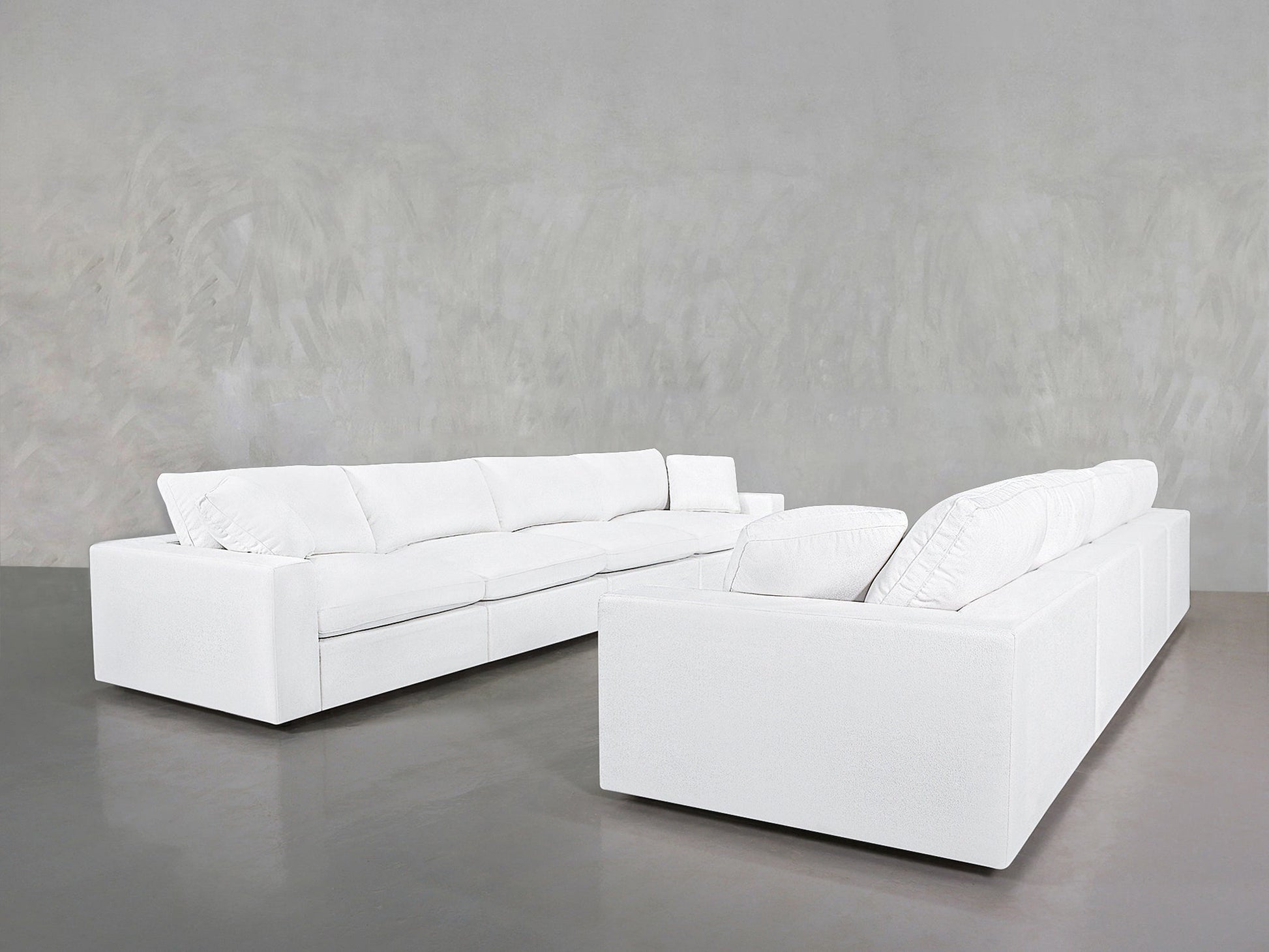 Two 4-4 Sofa Sets with modern white upholstery and plush cushions are arranged on a smooth grey floor, set against a light grey textured wall.