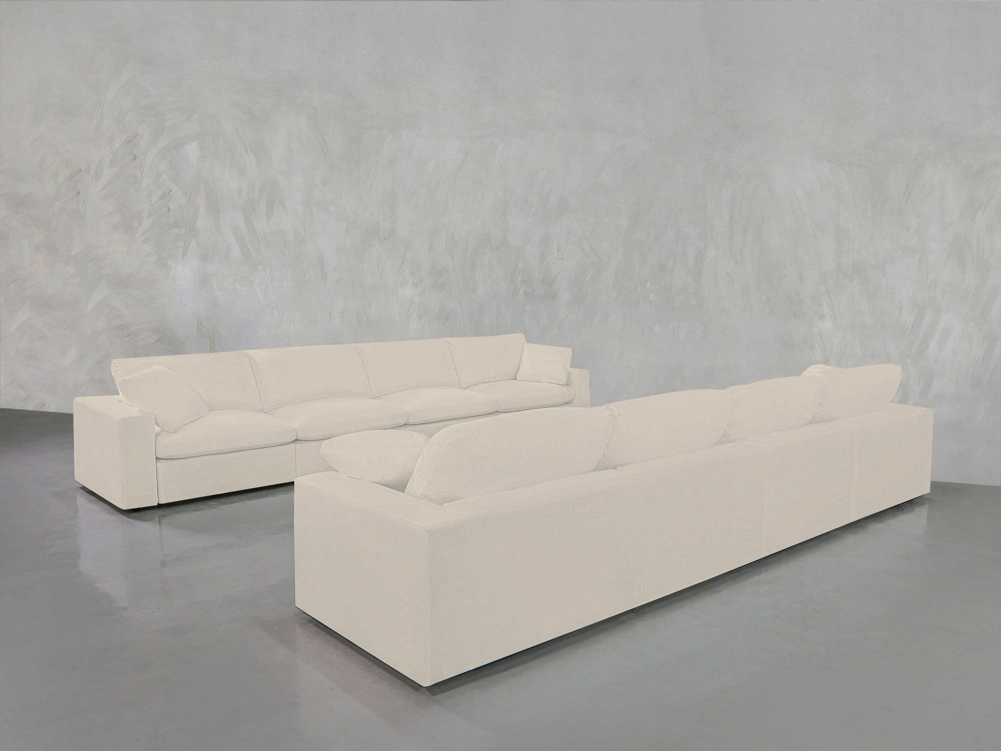 The 4-4 Sofa Set, featuring two large, modern white sofas with plush cushions, is arranged in an L-shape on a shiny gray floor against a light gray textured wall.