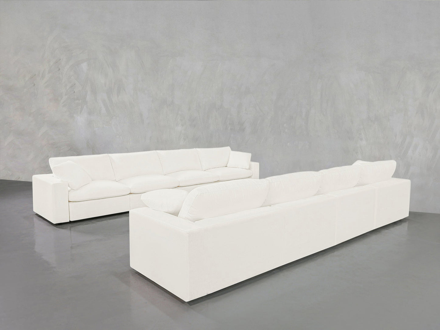 The 4-4 Sofa Set, featuring two modern white sofas with clean lines, is arranged facing each other in a minimalist room with a gray floor and textured gray walls for a symmetrical, contemporary look.