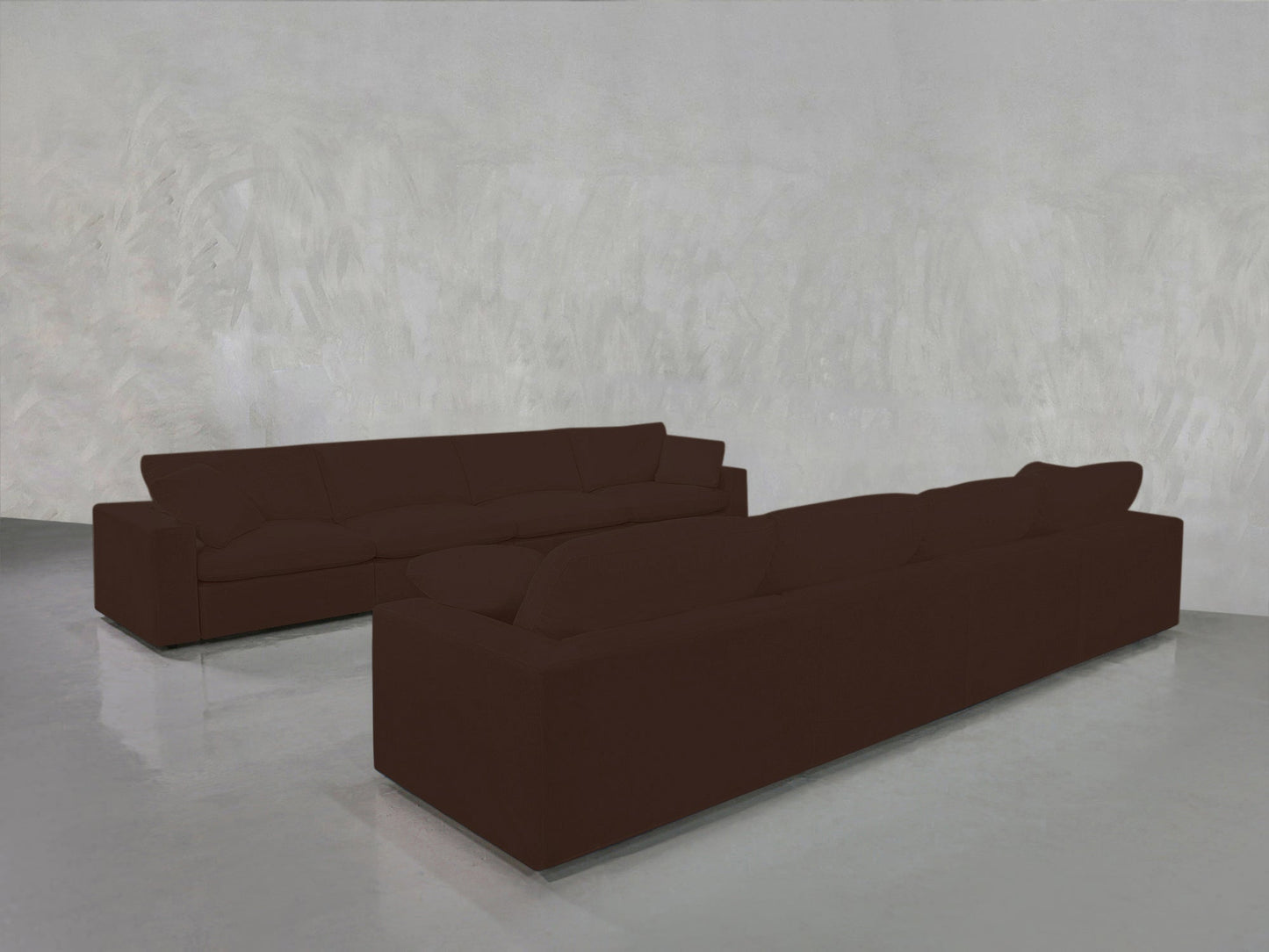 Two 4-4 Sofa Sets in dark brown are placed facing each other in a spacious room with light gray textured walls and a shiny, light gray floor.