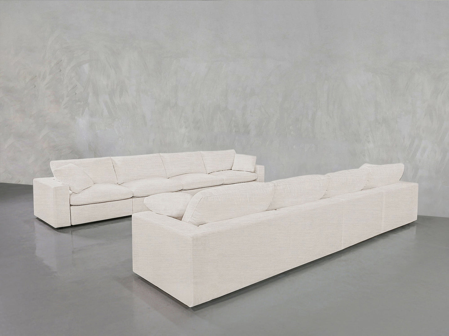 Two 4-4 Sofa Sets with modern white design, clean lines, and plush cushions are arranged in an L shape on a polished gray floor against a textured light gray wall.