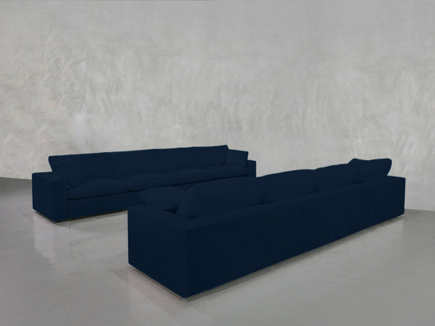 The 4-4 Sofa Set, featuring two dark blue modern sofas, is arranged in an L-shape in a minimalist space with grey textured walls and a polished light grey floor.