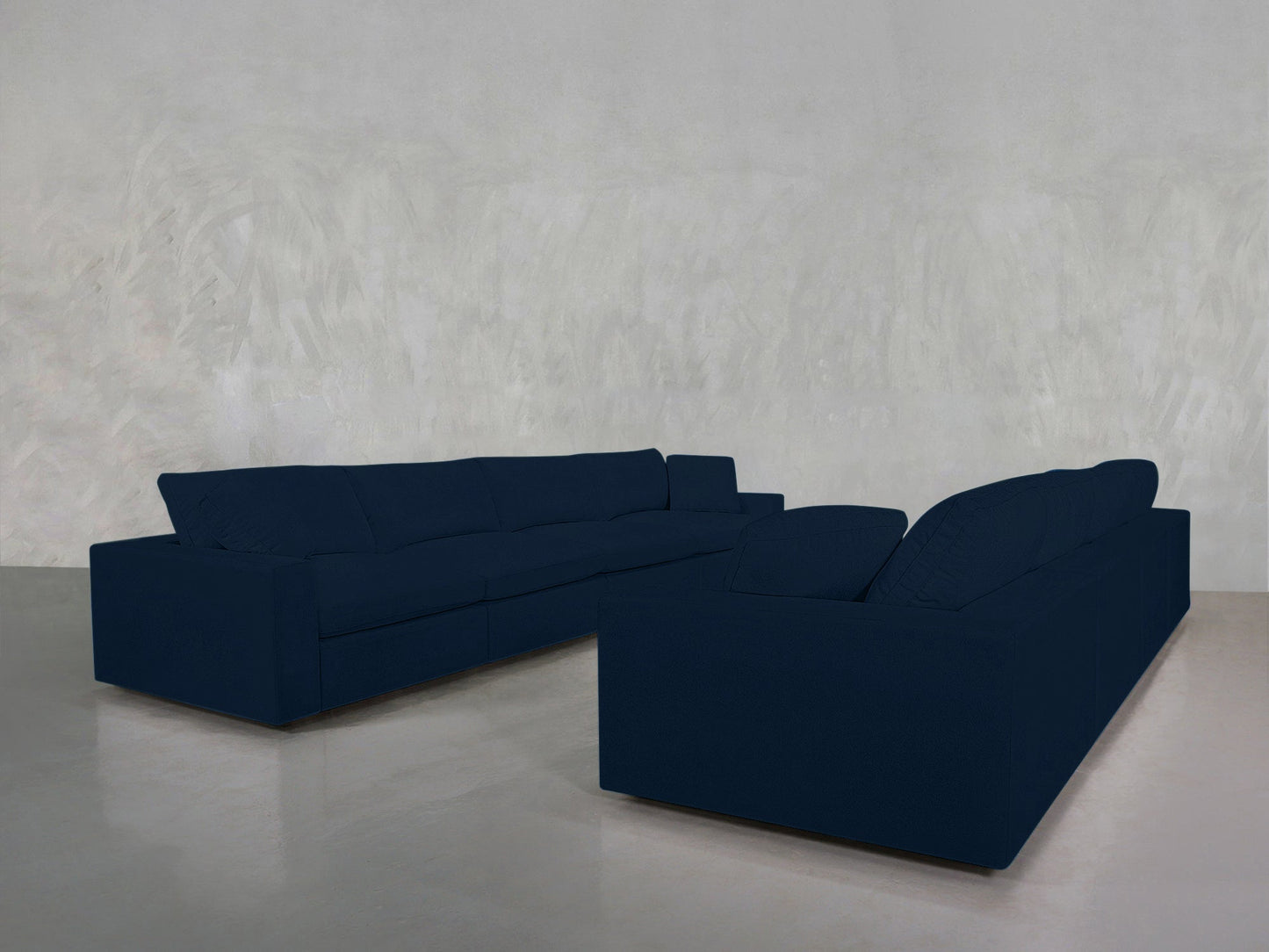 Two 4-4 Sofa Set sectional sofas in dark blue, arranged in an L-shape on a smooth light gray floor with a textured pale gray wall in the background.