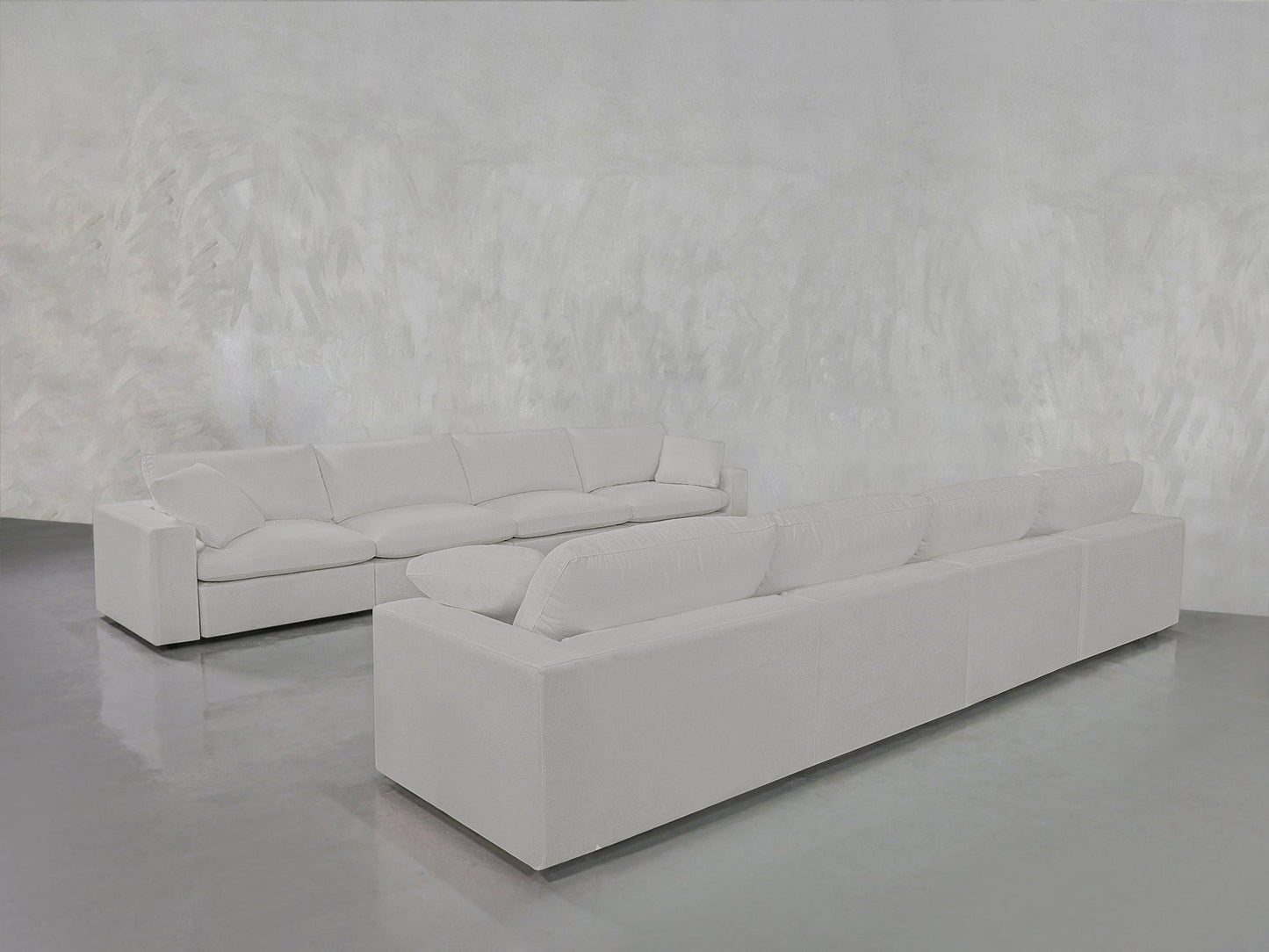 The 4-4 Sofa Set, featuring modern white sofas with plush cushions, is arranged on a shiny gray floor against a textured light gray wall for a minimalist and spacious look.