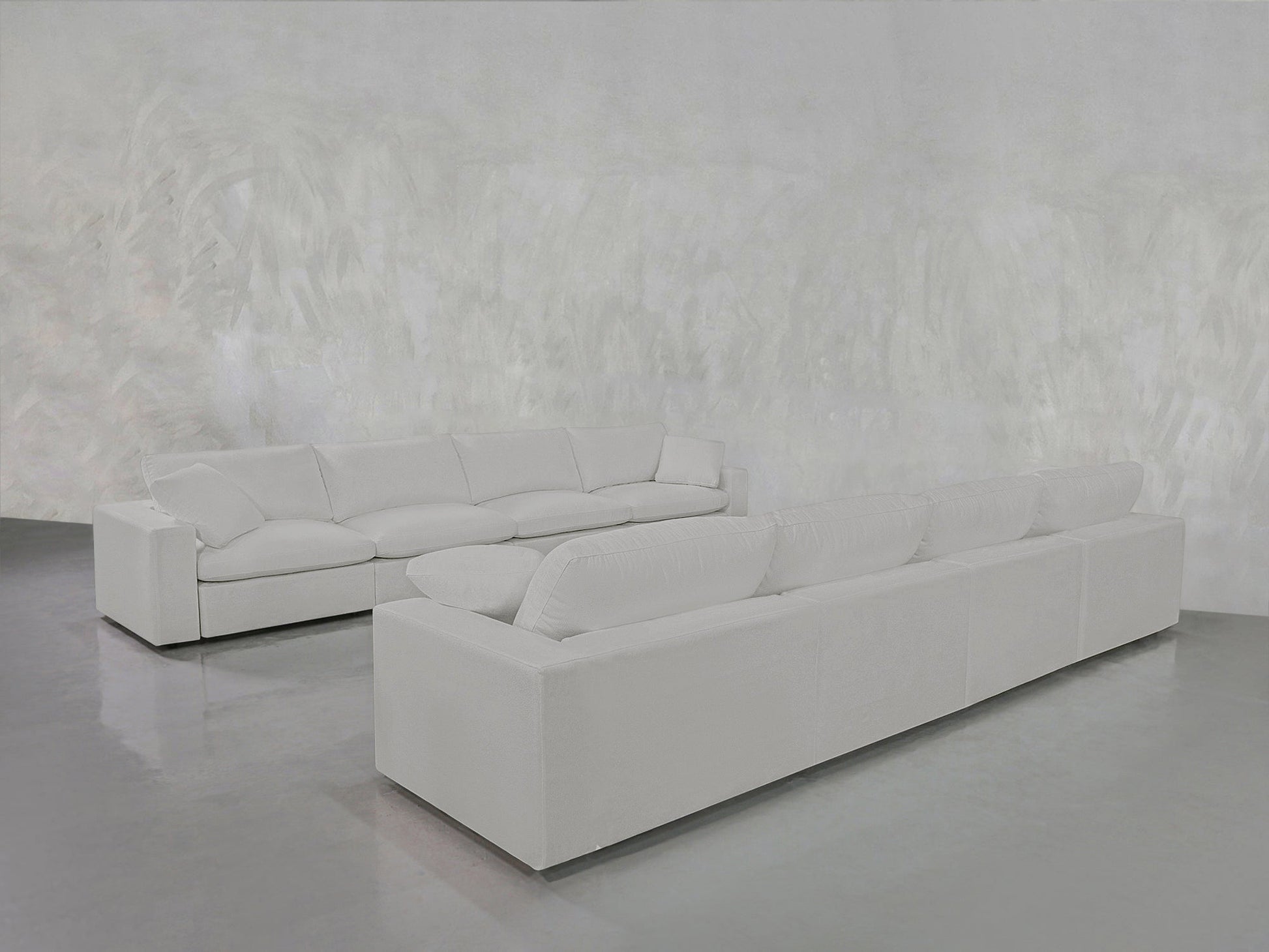 The 4-4 Sofa Set, featuring modern white sofas with plush cushions, is arranged on a shiny gray floor against a textured light gray wall for a minimalist and spacious look.
