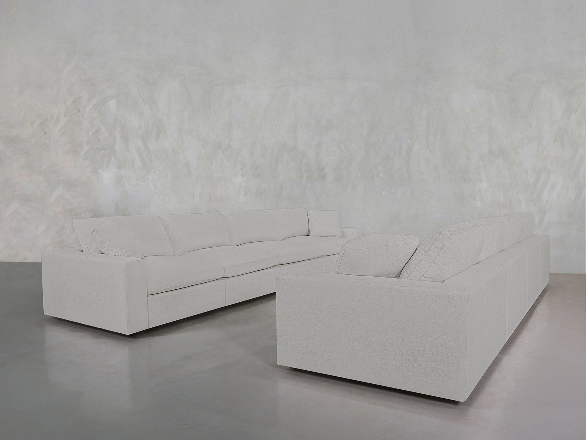 The 4-4 Sofa Set, in a large light gray L-shape, rests on a shiny gray floor in a minimalist room with textured pale gray walls, creating a modern and uncluttered space.