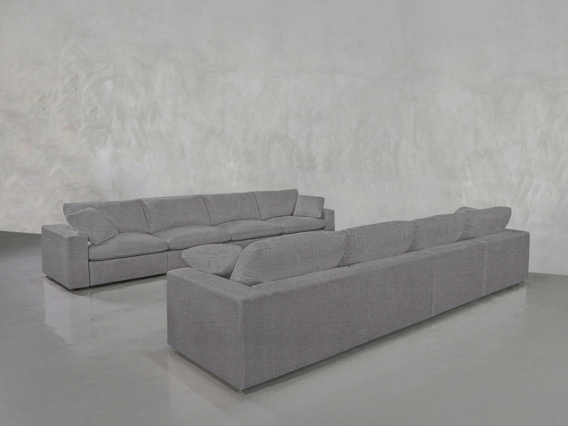 Two large, modern gray 4-4 Sofa Set sectionals with plush cushions are arranged in an L-shape on a shiny light gray floor against a textured light gray wall.