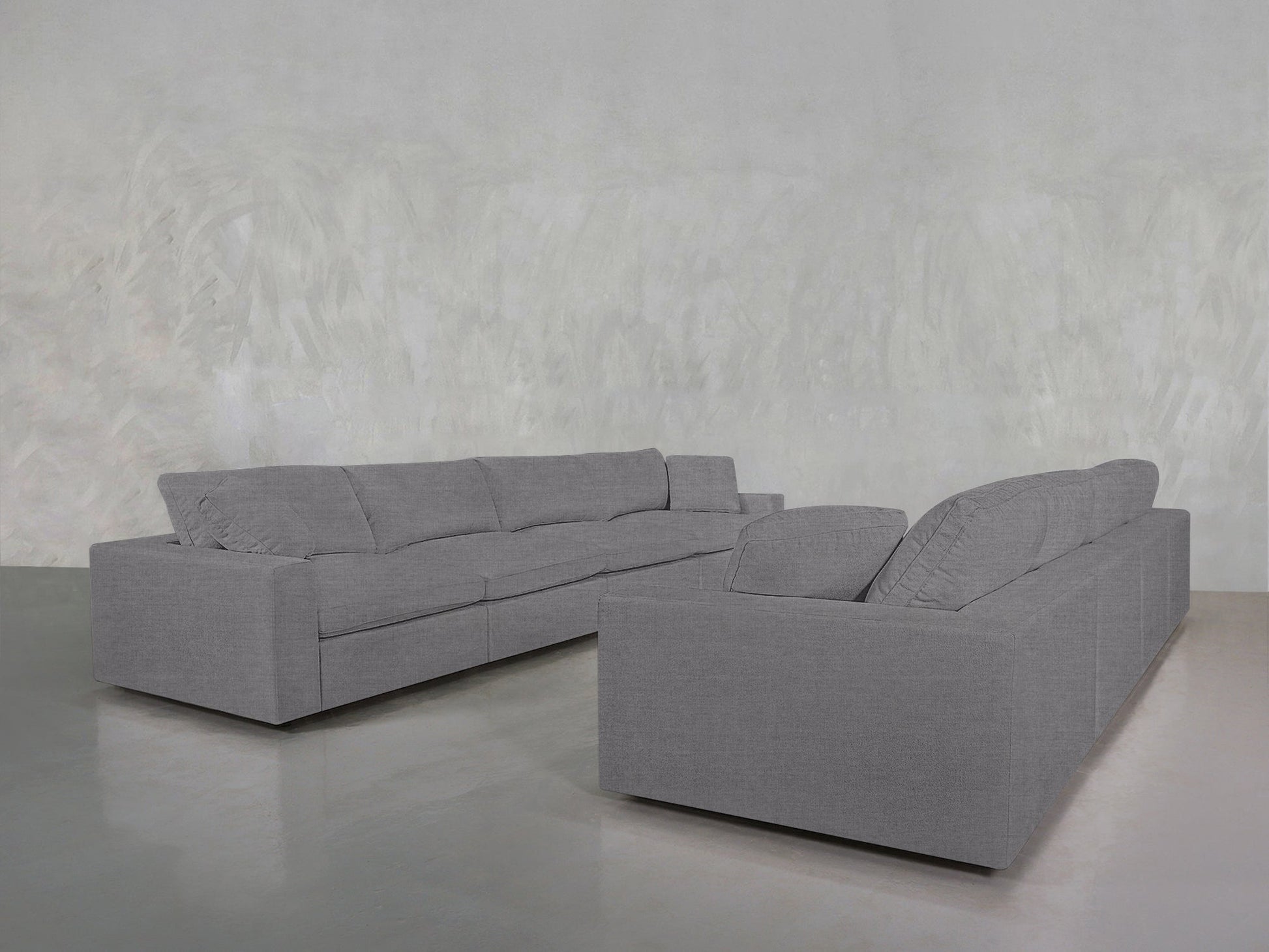 Two 4-4 Sofa Sets in gray are arranged in an L-shape in a minimalist room with light gray walls and a shiny, reflective floor.
