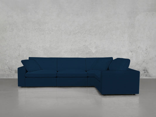 A 4-Seat Modular Corner Sectional in dark blue with clean lines and low backrests is set against a light gray textured wall on a smooth, light-colored floor.