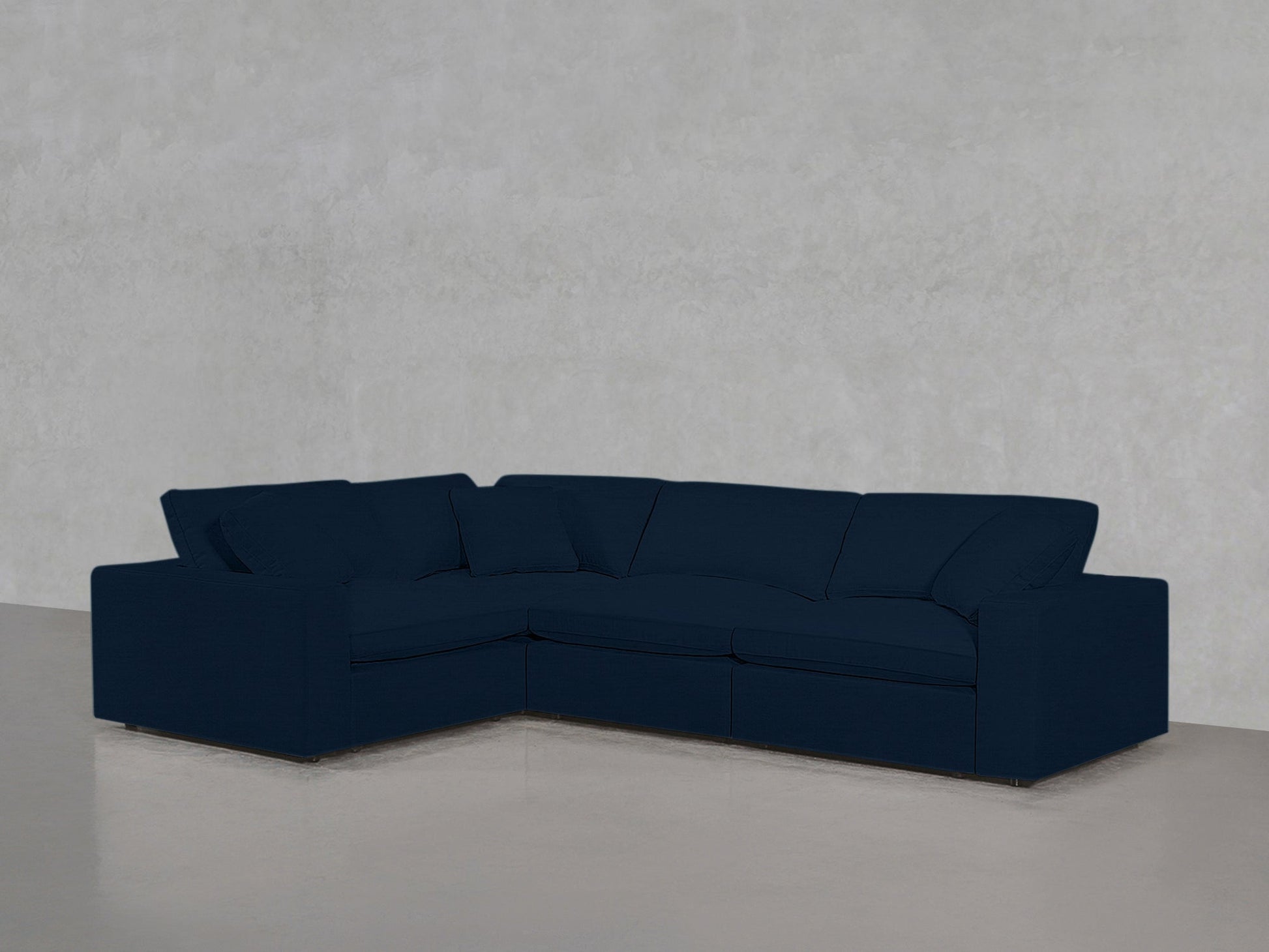 A 4-Seat Modular Corner Sectional in dark blue is positioned against a light gray textured wall on a smooth, light-colored floor.