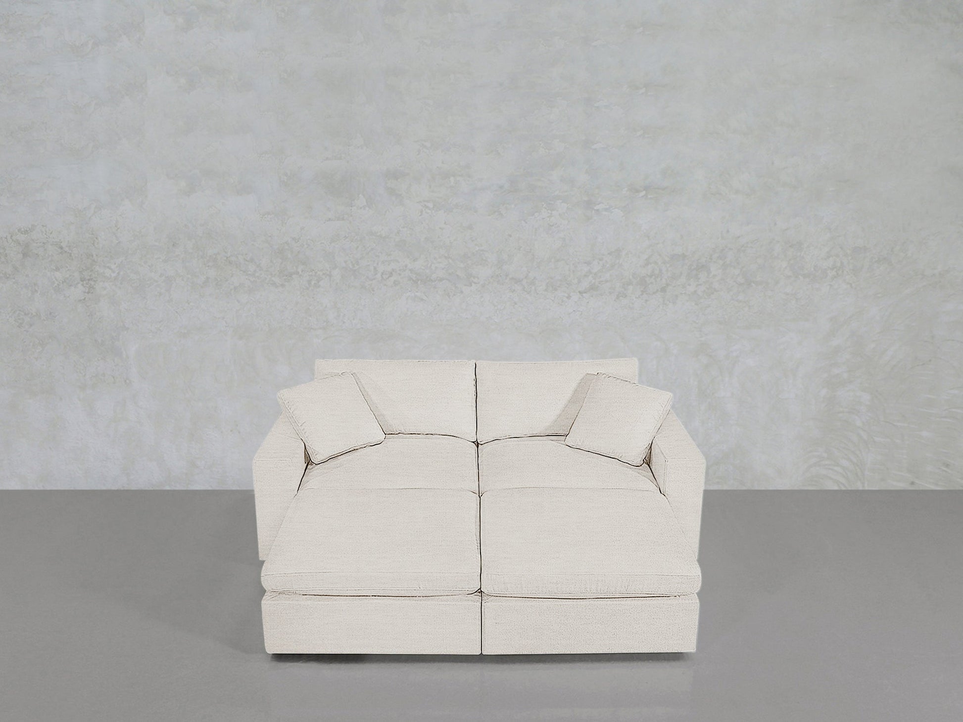 A modern, light beige 4-Seat Modular Daybed with two matching square cushions, set against a textured light gray wall and a smooth gray floor.