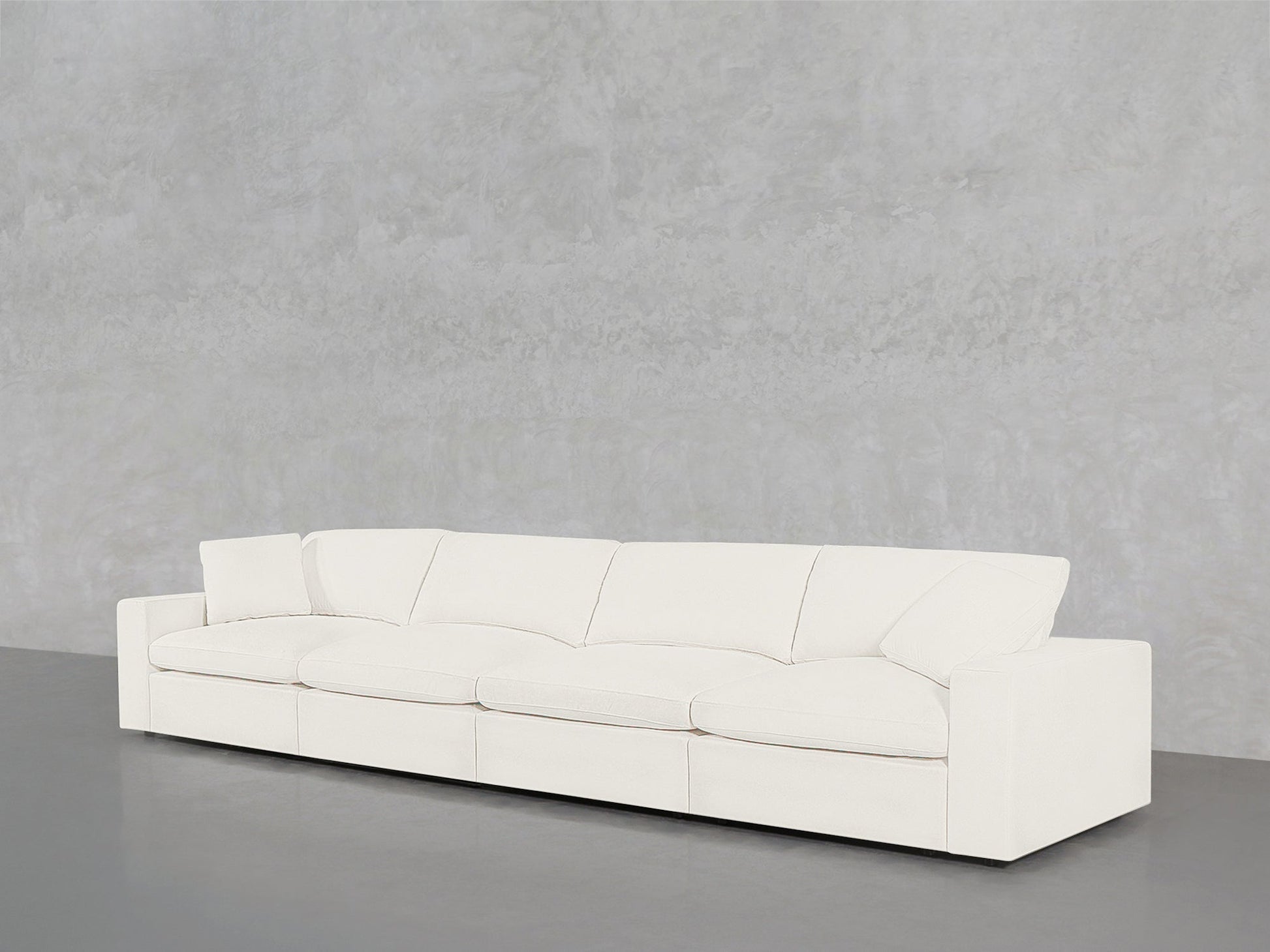 A 4-Seat Modular Sofa in modern white, featuring four seat and back cushions, stands against a plain light gray textured wall on a smooth gray floor.
