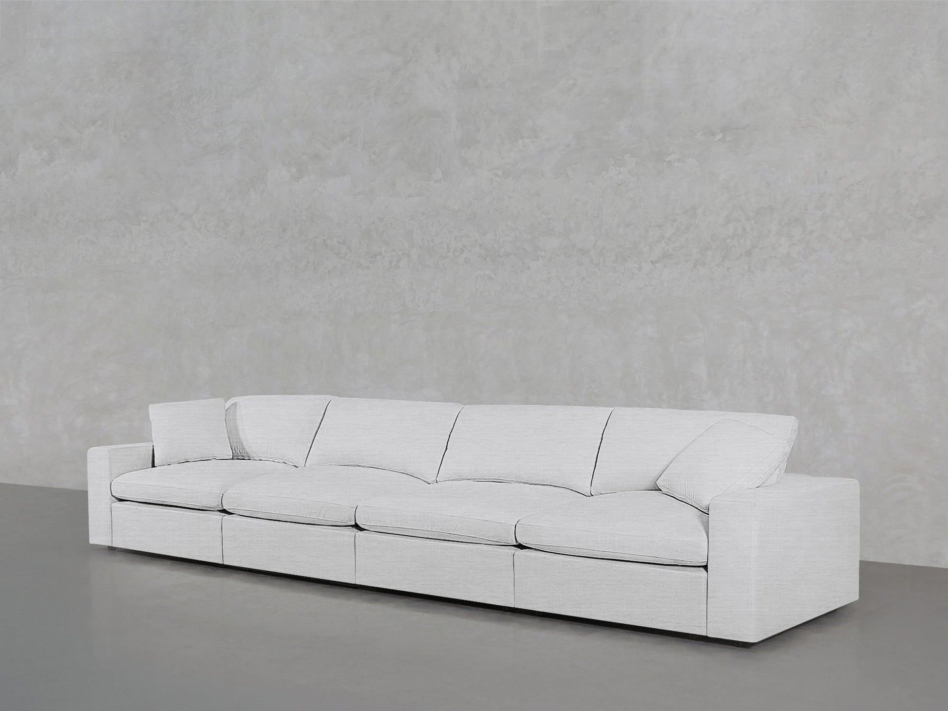 The 4-Seat Modular Sofa, modern and white with four seat cushions and two armrests, sits against a plain light gray textured wall on a smooth gray floor.