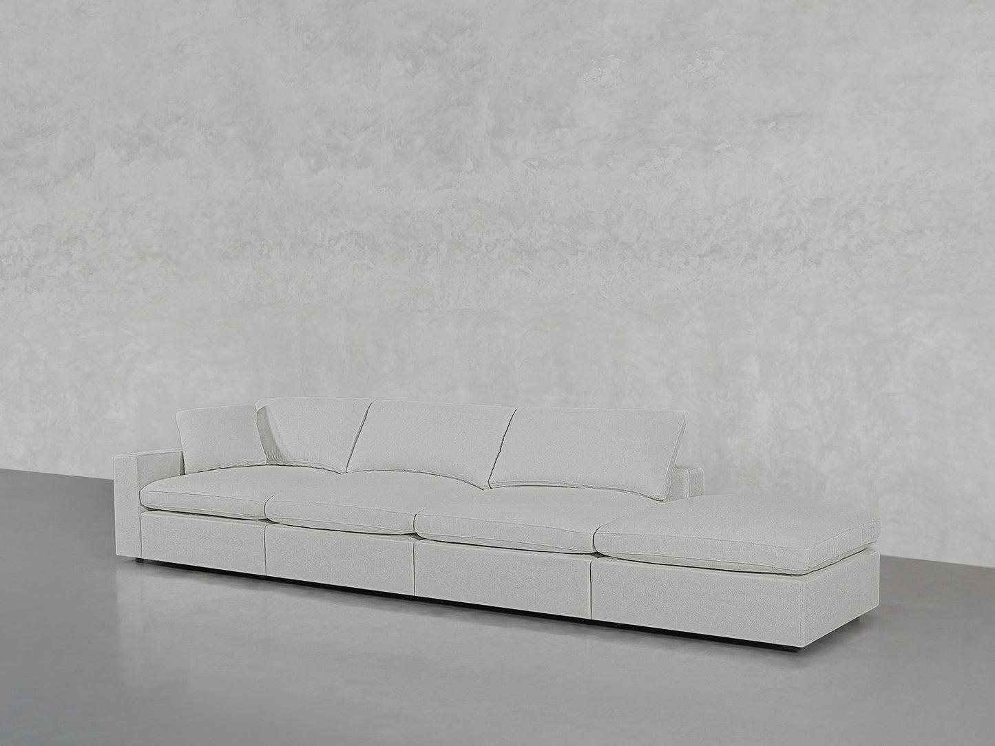 The 4-Seat Modular Lounger Sofa, in modern light gray with four cushions, is displayed against a plain textured light gray wall and a smooth gray floor.