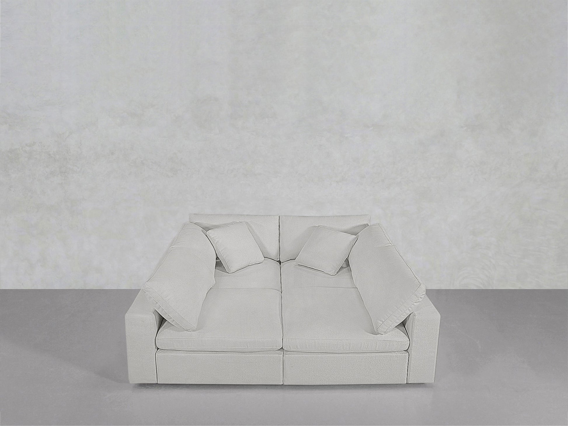 The 4-Seat Modular Pit, featuring wide armrests and four matching cushions, sits against a minimalist light gray wall and floor.