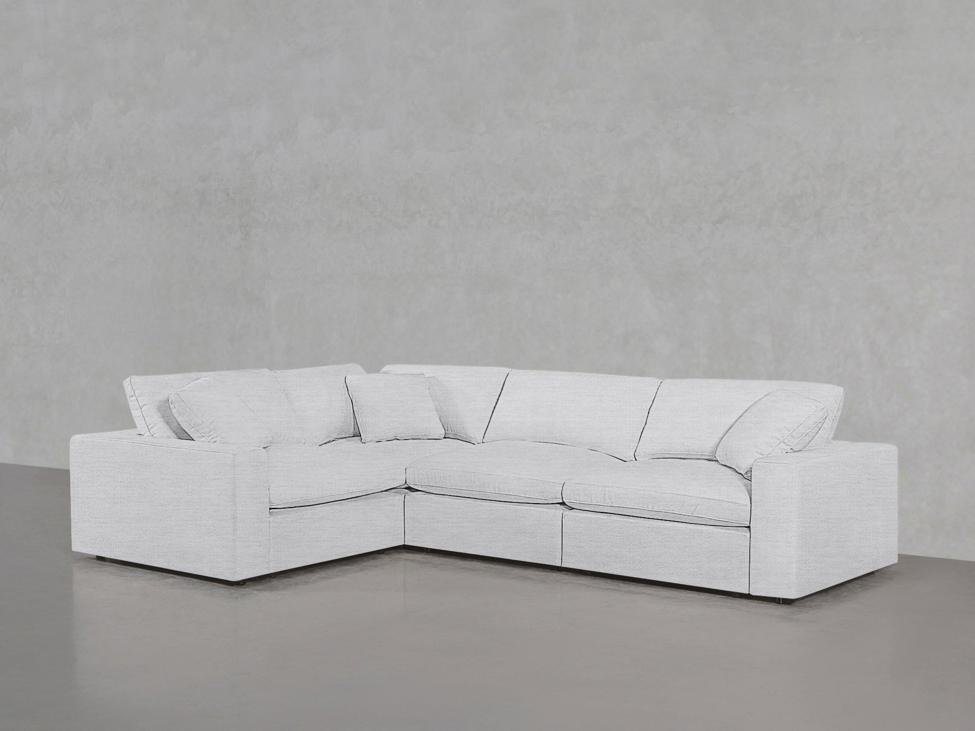 A 4-Seat Modular Corner Sectional in light gray with clean lines and plush cushions sits against a matching plain wall and floor in a minimalist setting.