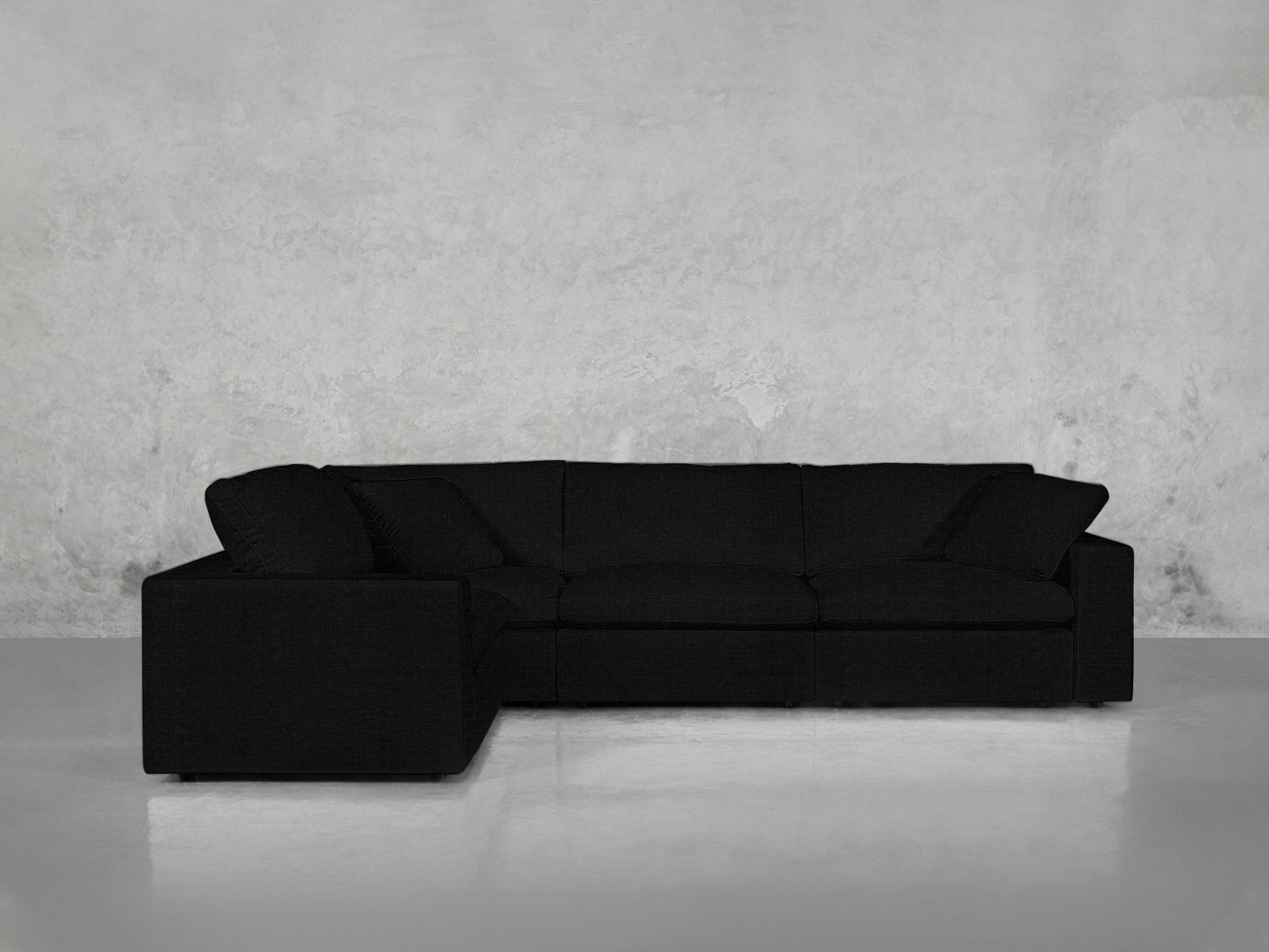 A 4-Seat Modular Corner Sectional with clean lines in modern black rests against a textured light gray wall on a smooth, light-colored floor.