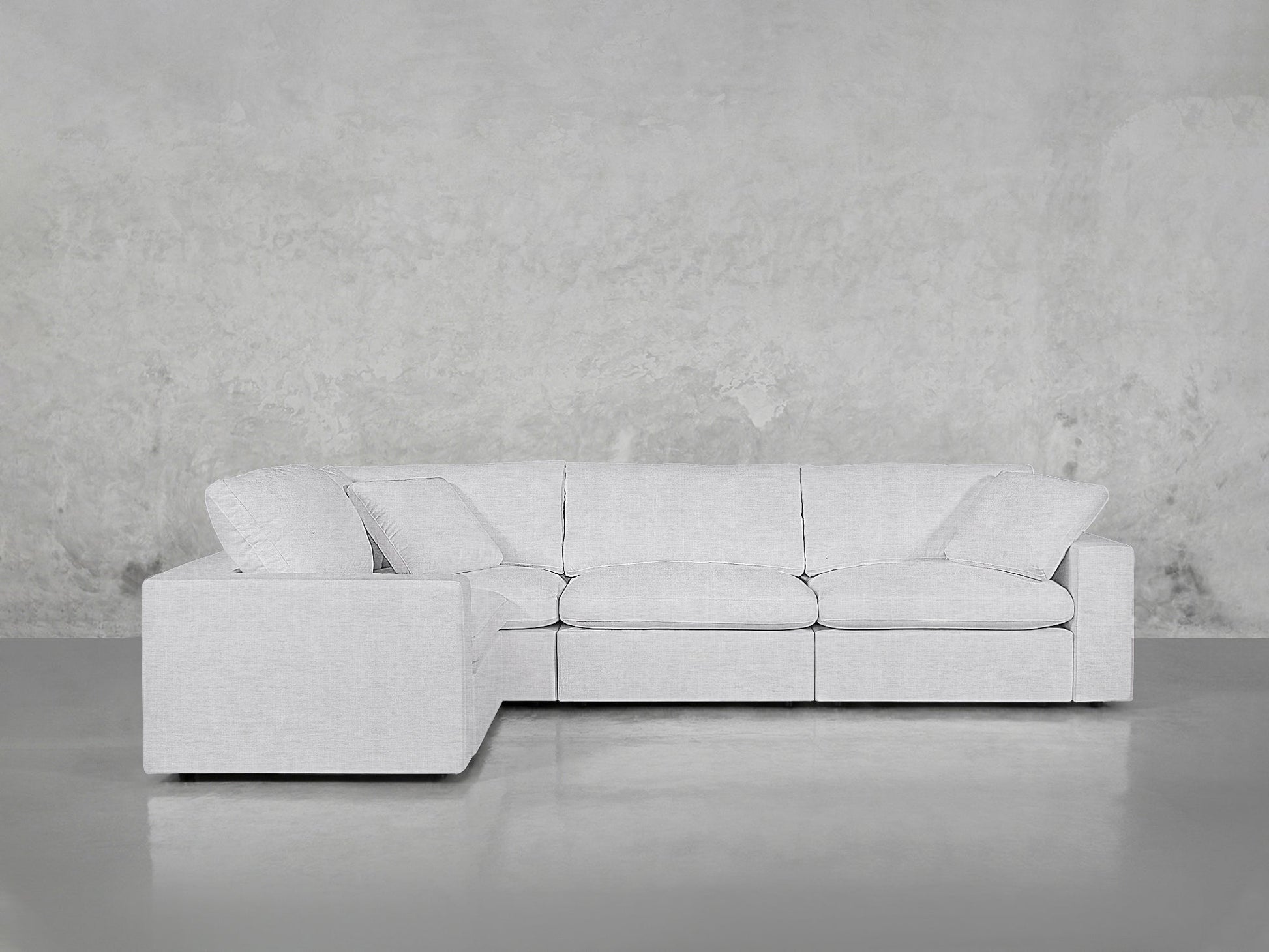 A modern 4-Seat Modular Corner Sectional in light gray, featuring three seat cushions and two back cushions, sits against a plain textured gray wall on a smooth, shiny floor.