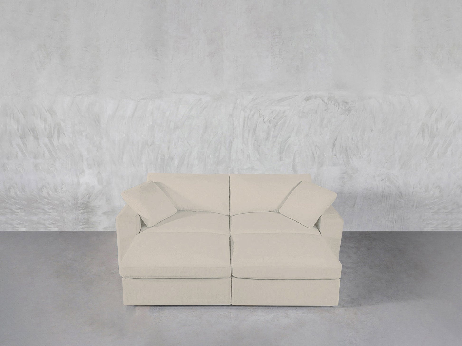 A modern light beige 4-Seat Modular Daybed with two matching cushions is placed against a textured light gray wall on a smooth gray floor.