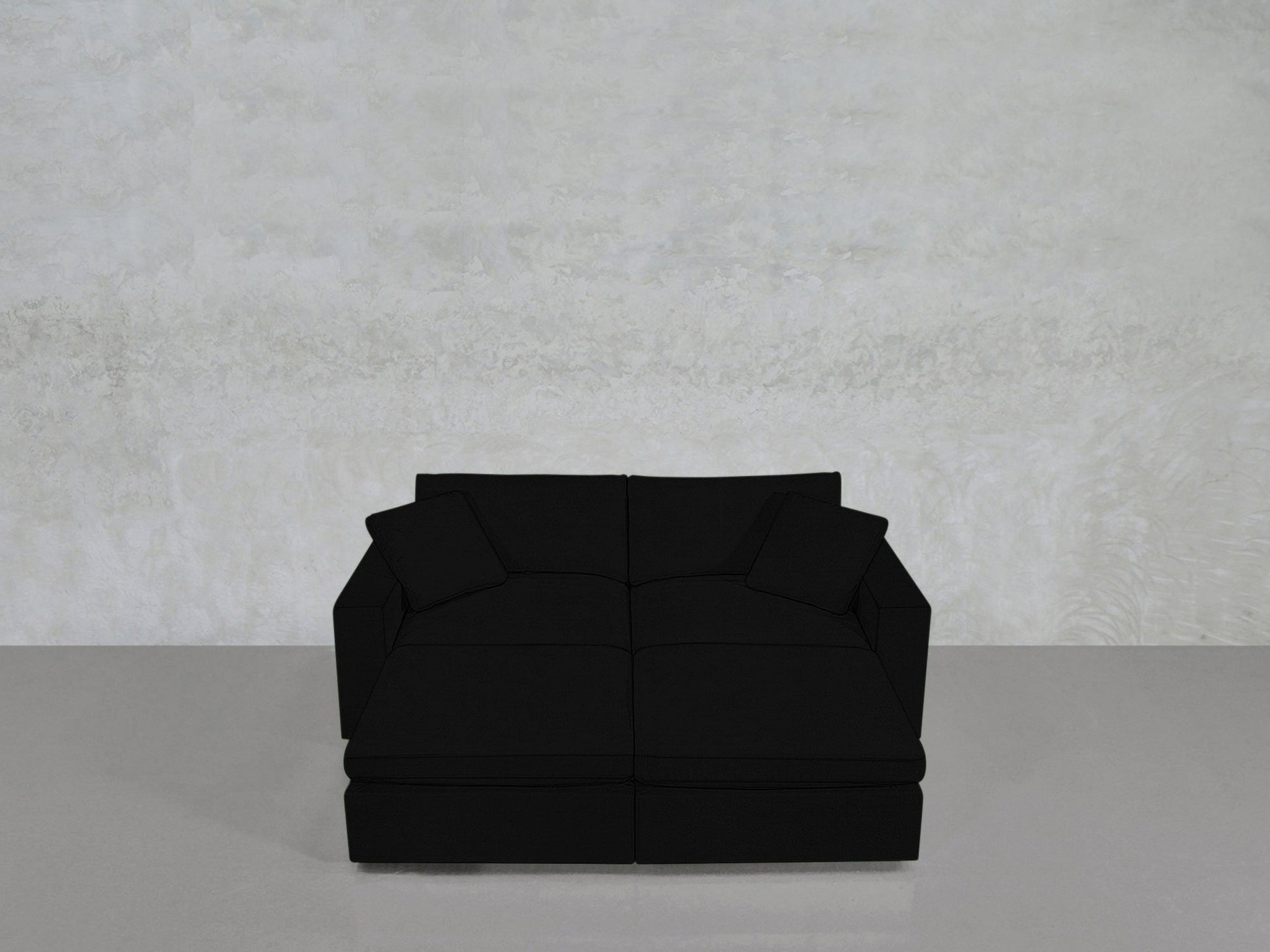 A contemporary 4-Seat Modular Daybed in black with two matching cushions rests on a glossy light gray floor against a textured light gray wall.