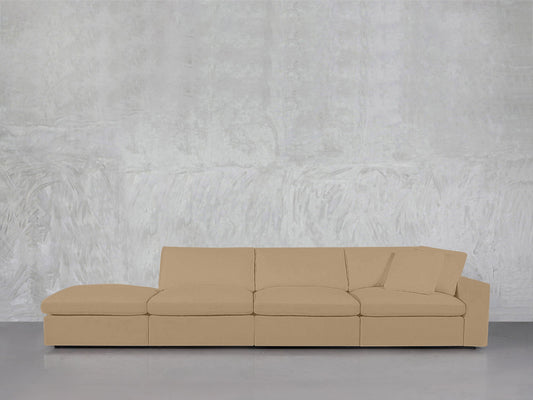 The 4-Seat Modular Lounger Sofa features a modern beige design with clean lines and a single matching cushion, set against a textured light gray wall and smooth gray floor.