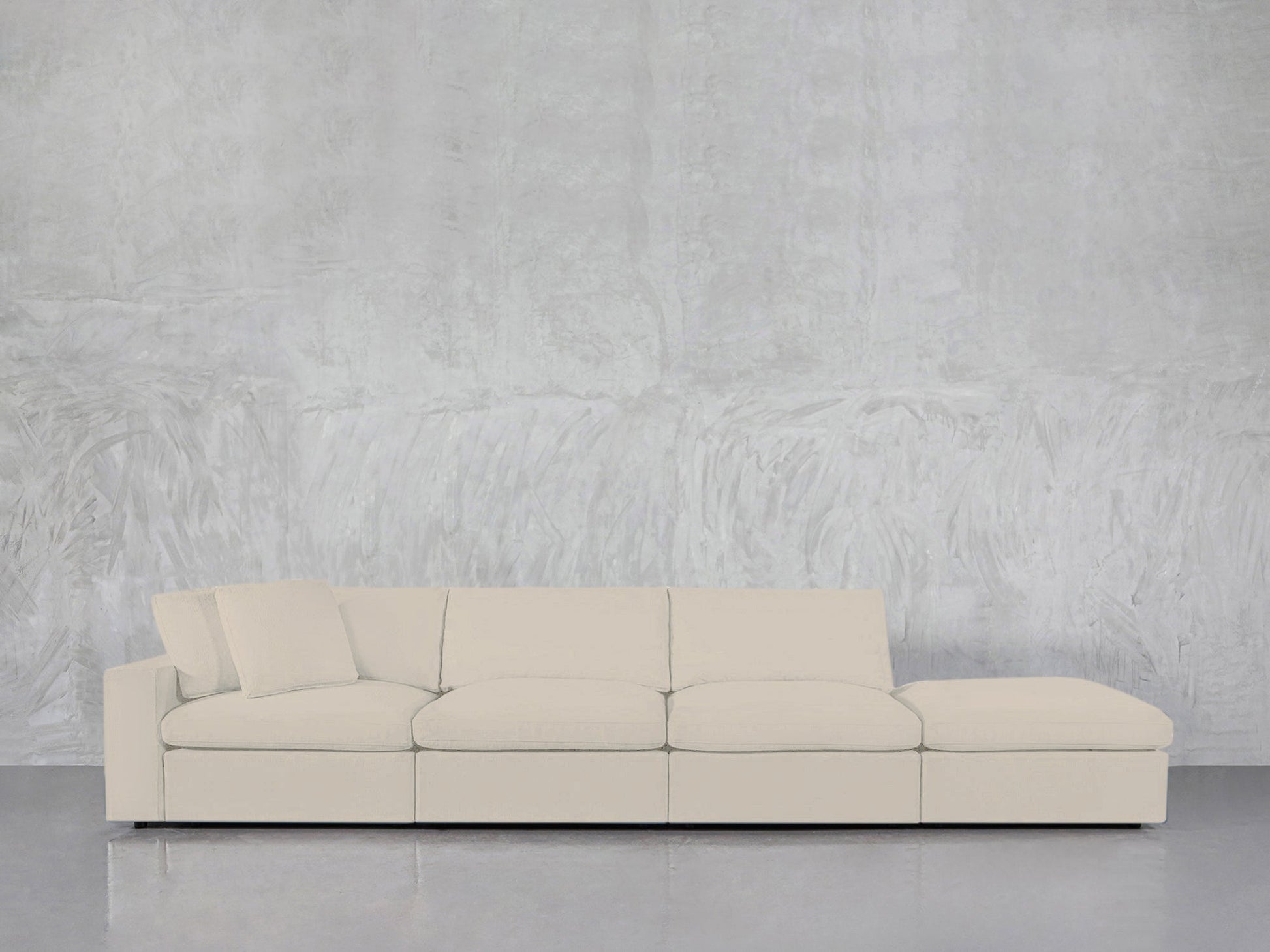 A modern 4-Seat Modular Lounger Sofa in light beige, featuring four seat cushions and one matching pillow, set against a textured pale gray wall on a shiny gray floor.