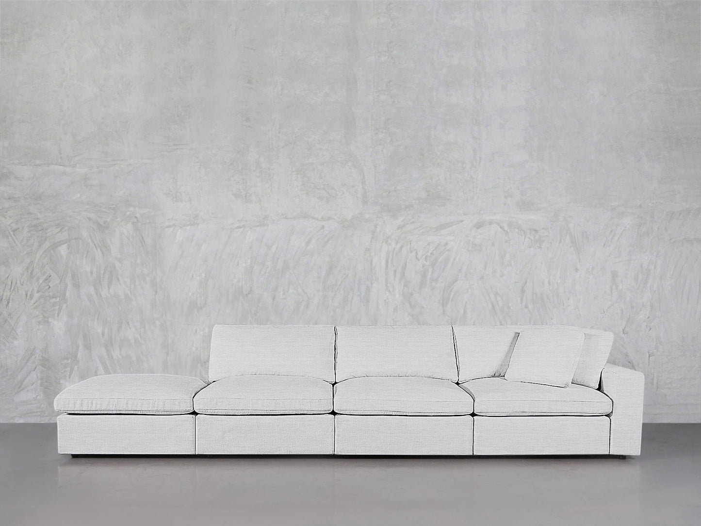 A modern 4-Seat Modular Lounger Sofa in light gray with matching pillow is set against a textured light gray wall on a polished concrete floor.