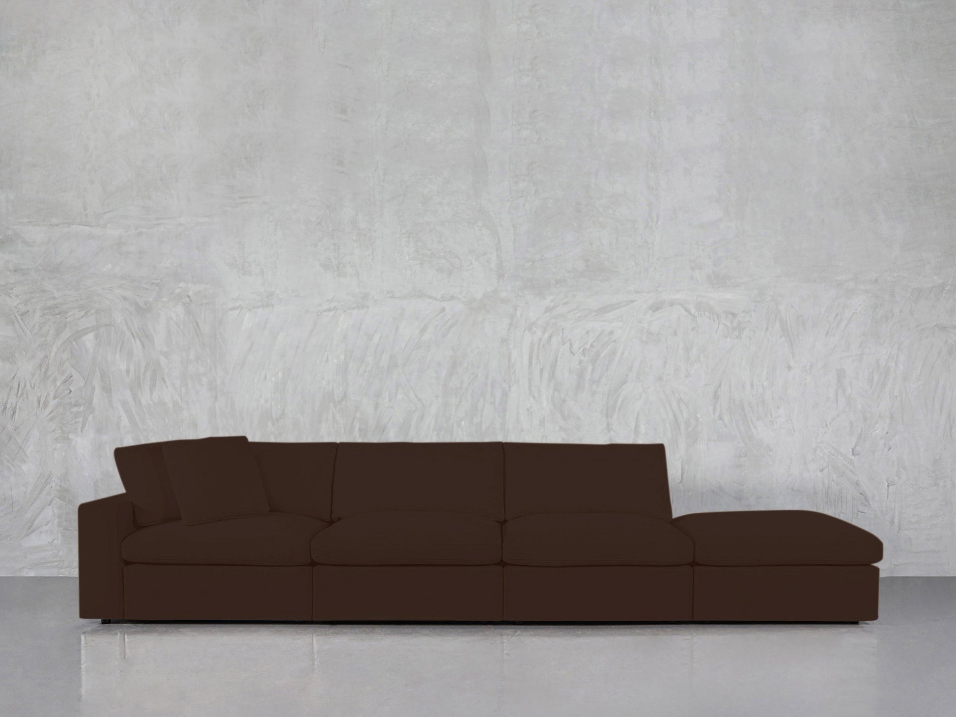 The 4-Seat Modular Lounger Sofa, featuring a modern design in dark brown with a low back and one armrest, is placed before a textured light gray wall and a shiny floor.