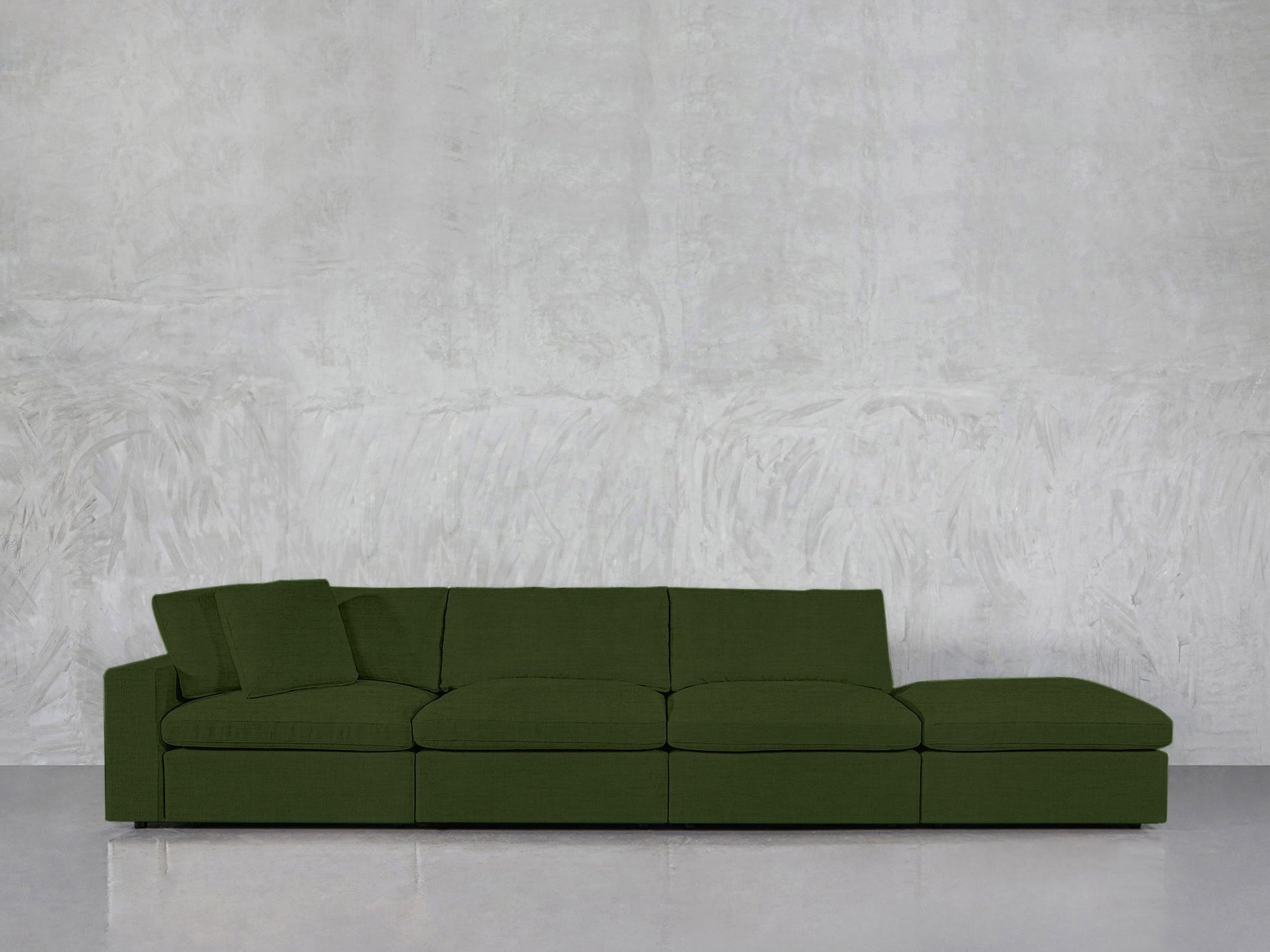 The 4-Seat Modular Lounger Sofa in green features four seats and a matching cushion, placed against a textured light gray wall and glossy gray flooring.