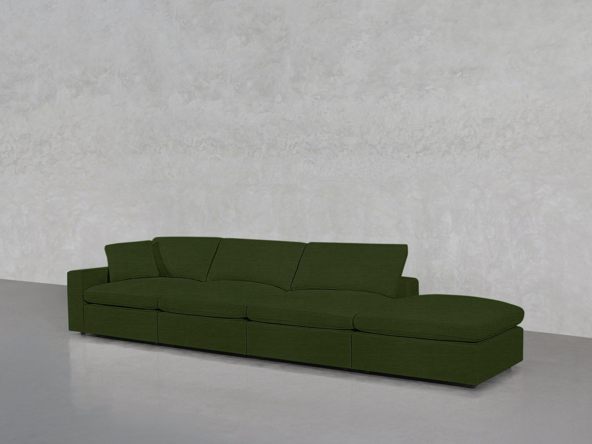 The 4-Seat Modular Lounger Sofa in green features wide cushions and a right-side chaise, set against a plain light gray textured wall and floor.