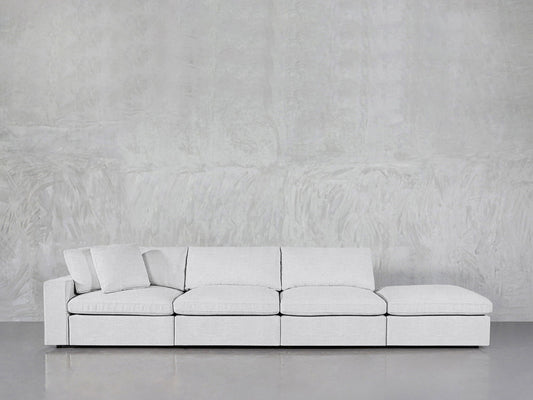 The 4-Seat Modular Lounger Sofa in light gray features four square seat cushions and one matching pillow, showcased against a textured gray wall and a smooth gray floor.