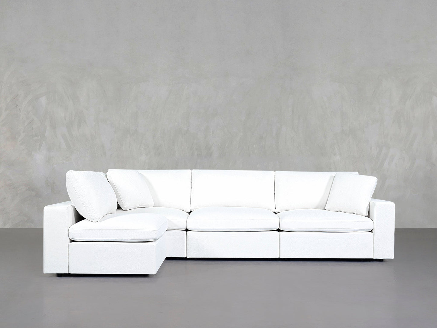 A 4-Seat Modular Open Corner Sectional with clean lines and white upholstery is placed against a light gray textured wall and gray floor.