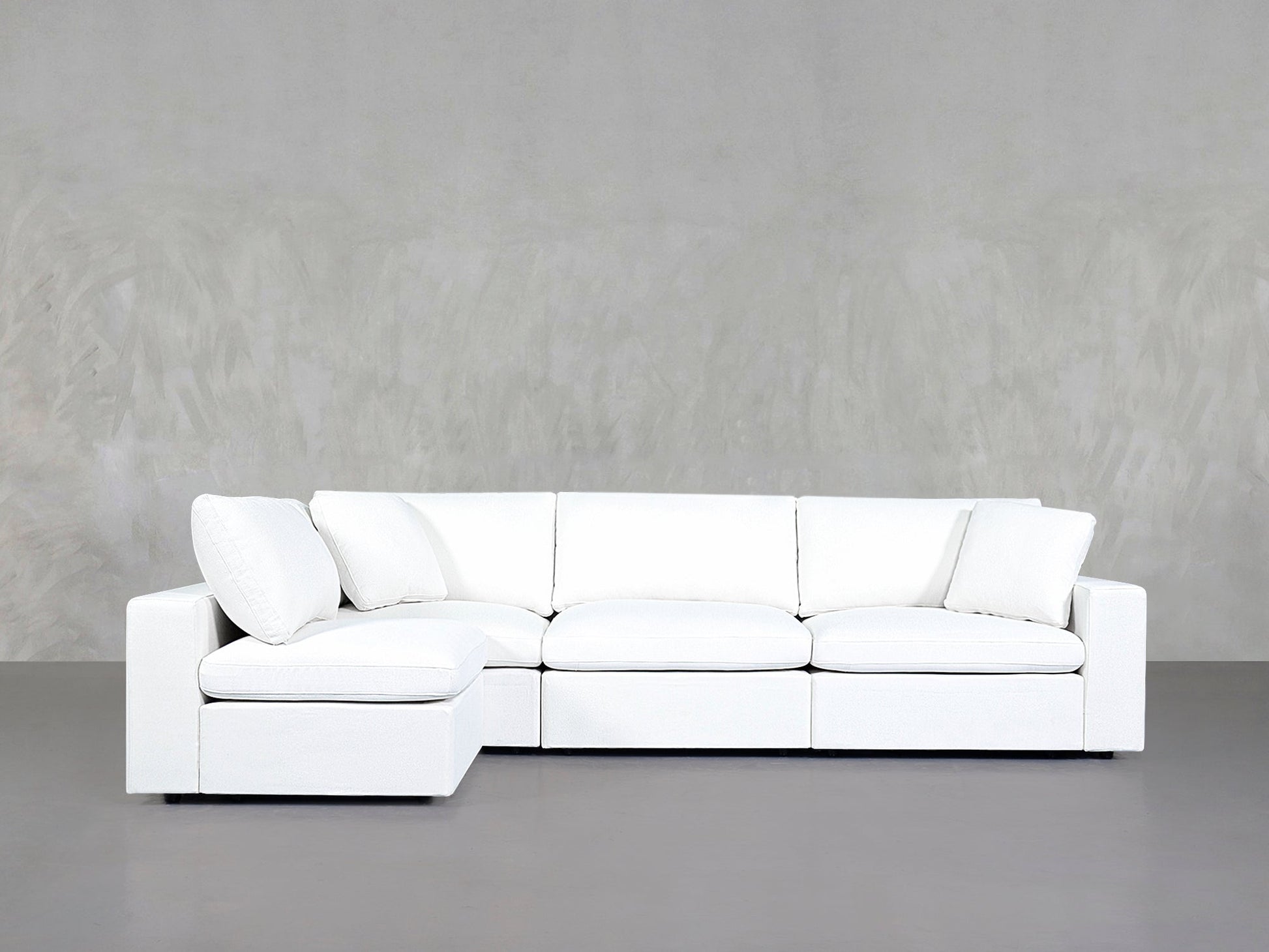 A 4-Seat Modular Open Corner Sectional with clean lines and white upholstery is placed against a light gray textured wall and gray floor.