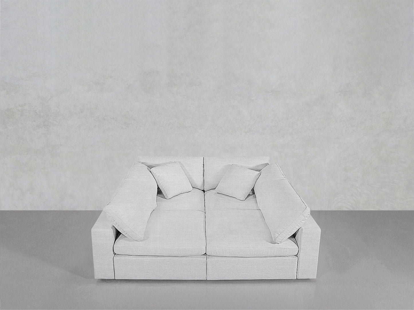 A light gray, modern 4-Seat Modular Pit sofa with wide armrests and four matching cushions is placed against a plain, light gray wall on a smooth gray floor.