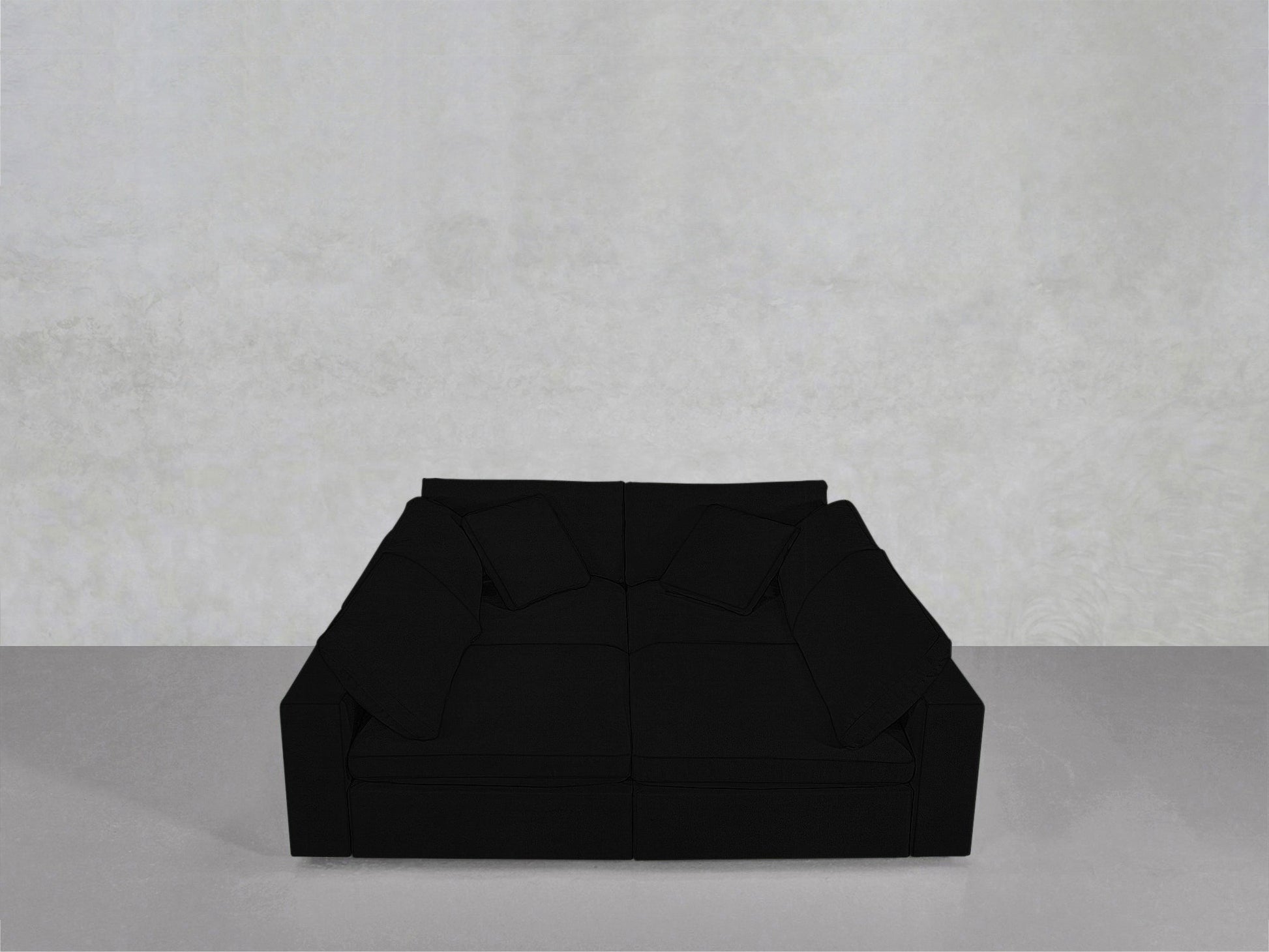 The 4-Seat Modular Pit, a large modern black sofa with four matching cushions, sits on a grey floor against a plain light grey wall.