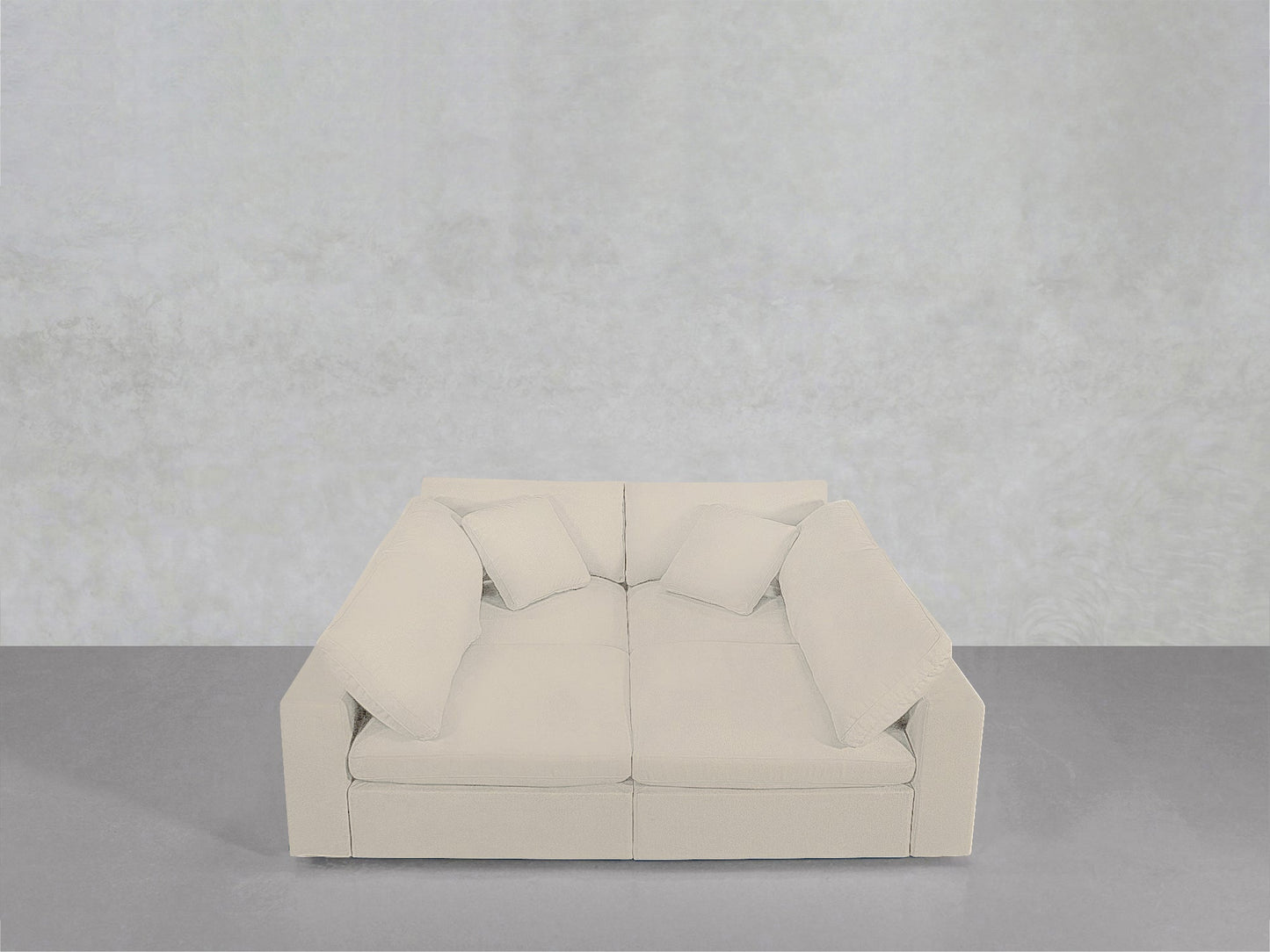 A modern, light beige 4-Seat Modular Pit with four matching cushions is set against a plain, light gray wall on a smooth gray floor.