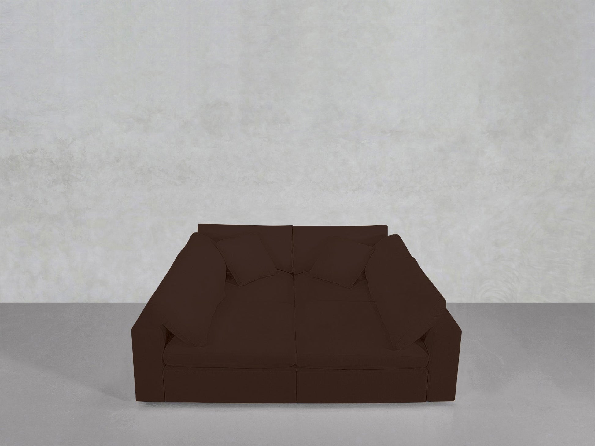 A dark brown 4-Seat Modular Pit with cushions is positioned against a plain, light gray wall on a smooth gray floor.