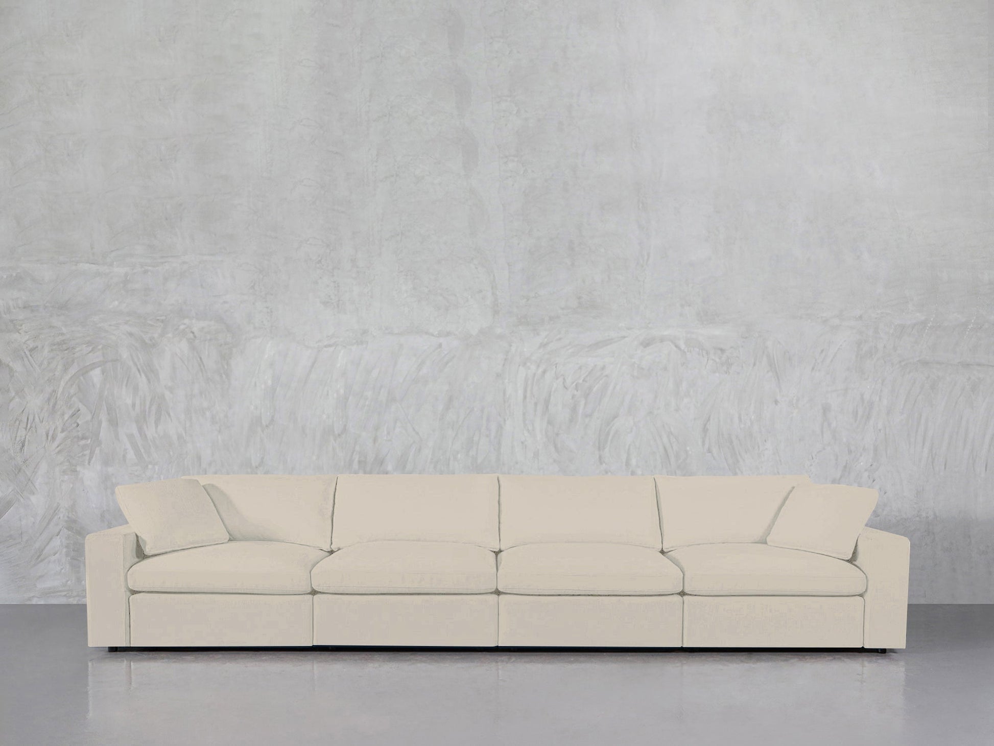 A modern cream-colored 4-Seat Modular Sofa stands against a textured light gray wall on a polished, reflective floor.