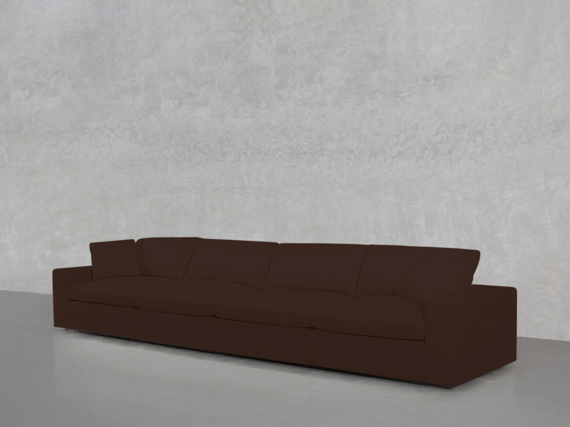 The 4-Seat Modular Sofa in dark brown, featuring four seat cushions and wide armrests, sits against a light gray textured wall on a smooth gray floor.