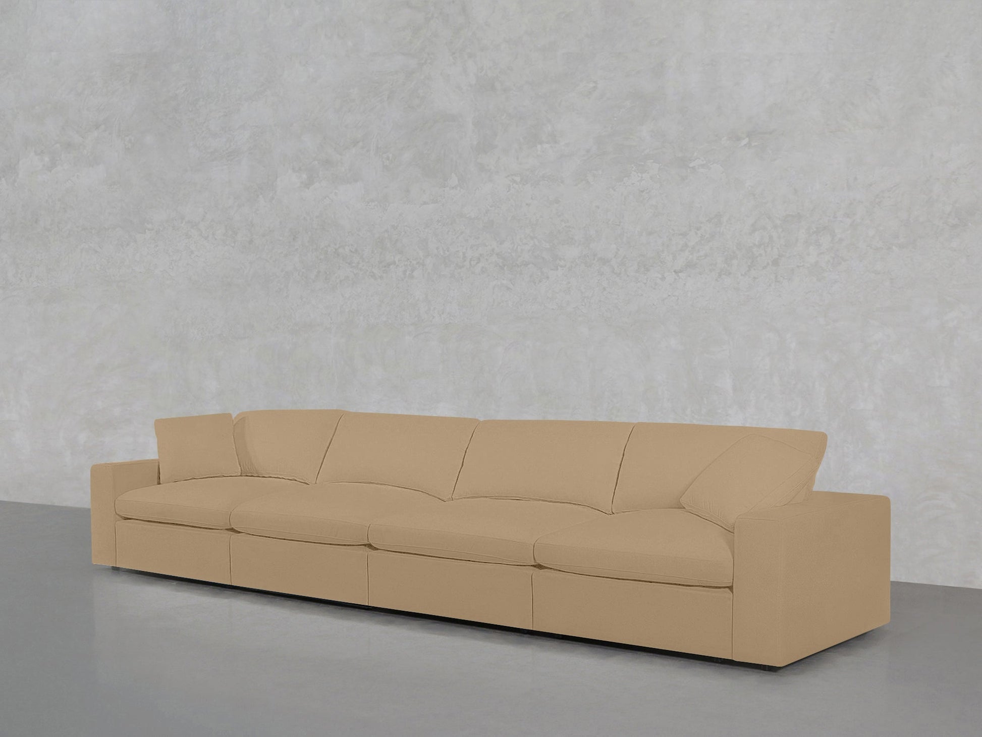 The 4-Seat Modular Sofa, beige and modern with four seat and back cushions, is placed against a light gray textured wall on a gray floor.