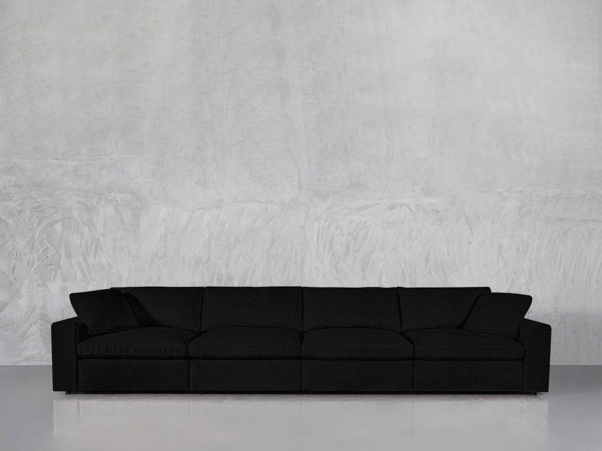 A 4-Seat Modular Sofa in black with a modern design sits against a light gray textured wall on a shiny, reflective floor in a minimalist setting.