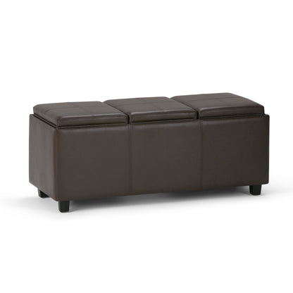 The Avalon Upholstered Storage Ottoman is a rectangular, dark brown faux leather piece with three cushioned sections and short black legs, shown on a white background.