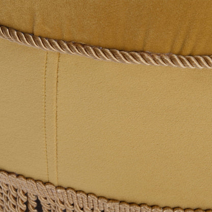 Close-up of the Yolanda - Luxurious Upholstery Round Upholstered Accent Ottoman in mustard yellow fabric, featuring a stitched seam, twisted cord trim, and fringed trim along the bottom edge.