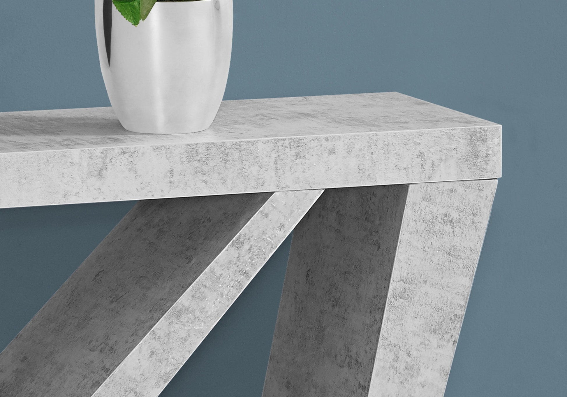 The Accent Console Table For Entryway, featuring durable construction and angled legs, stands against a blue wall with a silver vase of green leaves placed on top.