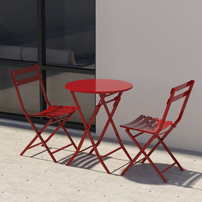 The 3 Piece Patio Bistro Set of Foldable Round Table and Chairs, in red metal, is arranged on a concrete patio beside a white wall and large window.
