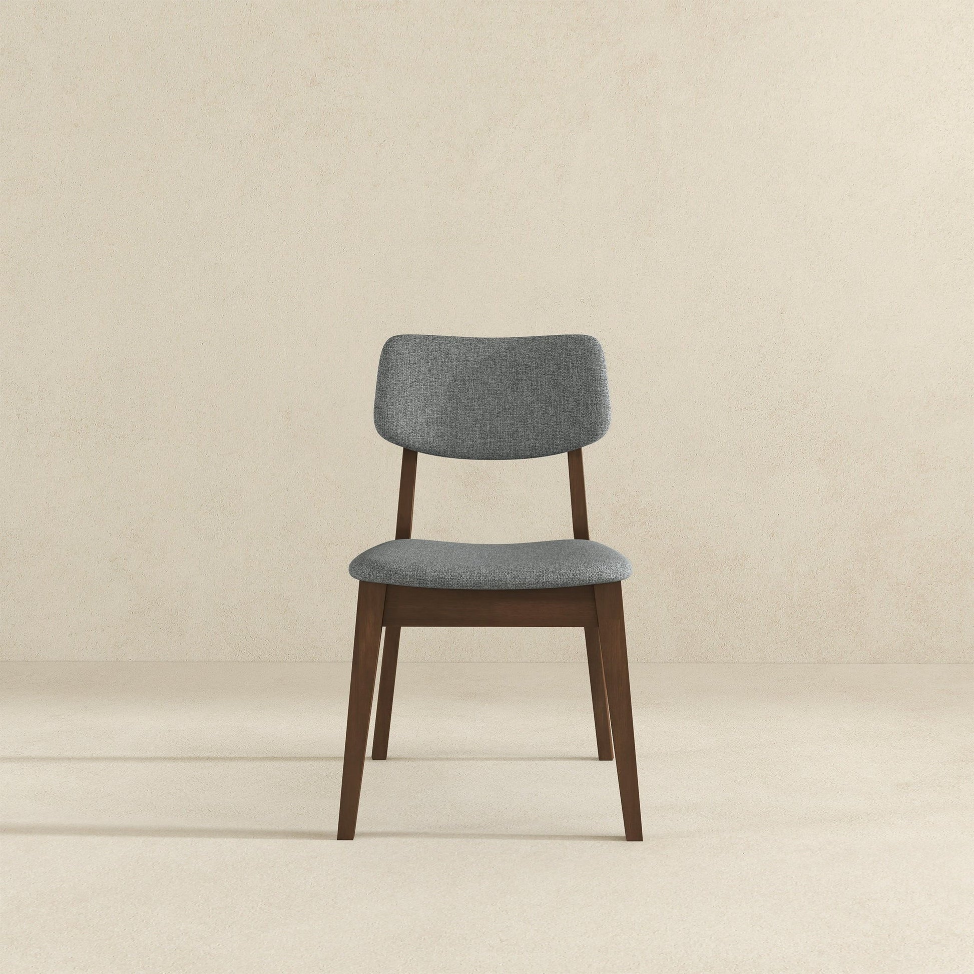 The Carlos Solid Back Side Chair (Set of 2) features a cushioned gray fabric seat and backrest with dark wooden legs and frame, shown against a plain beige background.