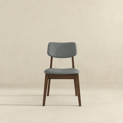 The Carlos Solid Back Side Chair (Set of 2) features a cushioned gray fabric seat and backrest with dark wooden legs and frame, shown against a plain beige background.