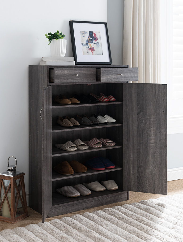 A Shoe Storage Cabinet with five shelves and two drawers fits 15 pairs of shoes. Its open door displays slippers on the shelves, with a picture frame and potted plant on top, and it's placed by a window with white curtains and a lantern nearby.