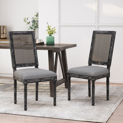 Two French Country Dining Chairs with rectangular cane backs and smooth upholstered gray seats sit on a light patterned rug near a dark wooden table with a green vase and plants in a bright, modern room.